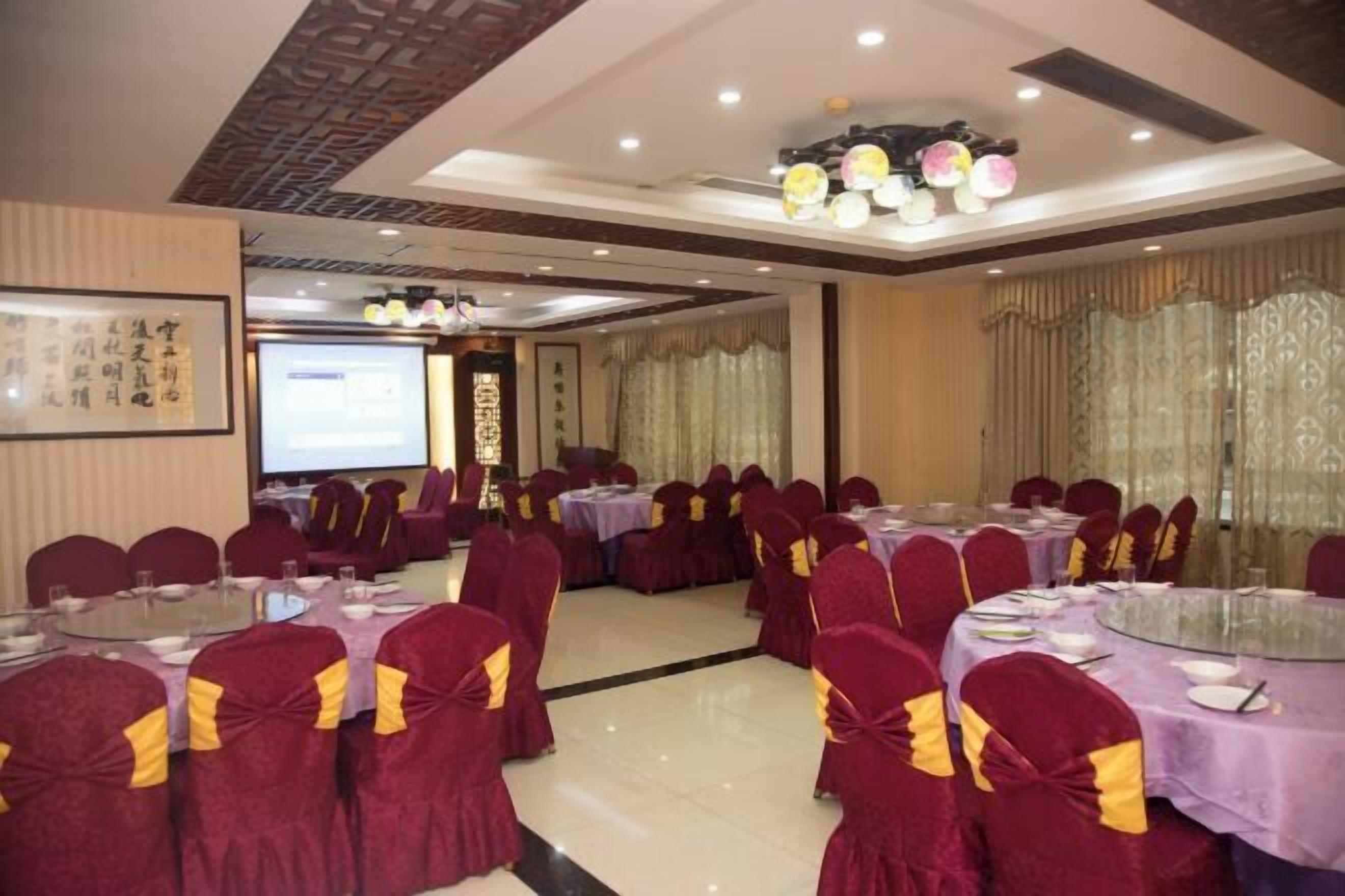 A conference room with round tables, chairs with yellow sashes, and a projector screen.