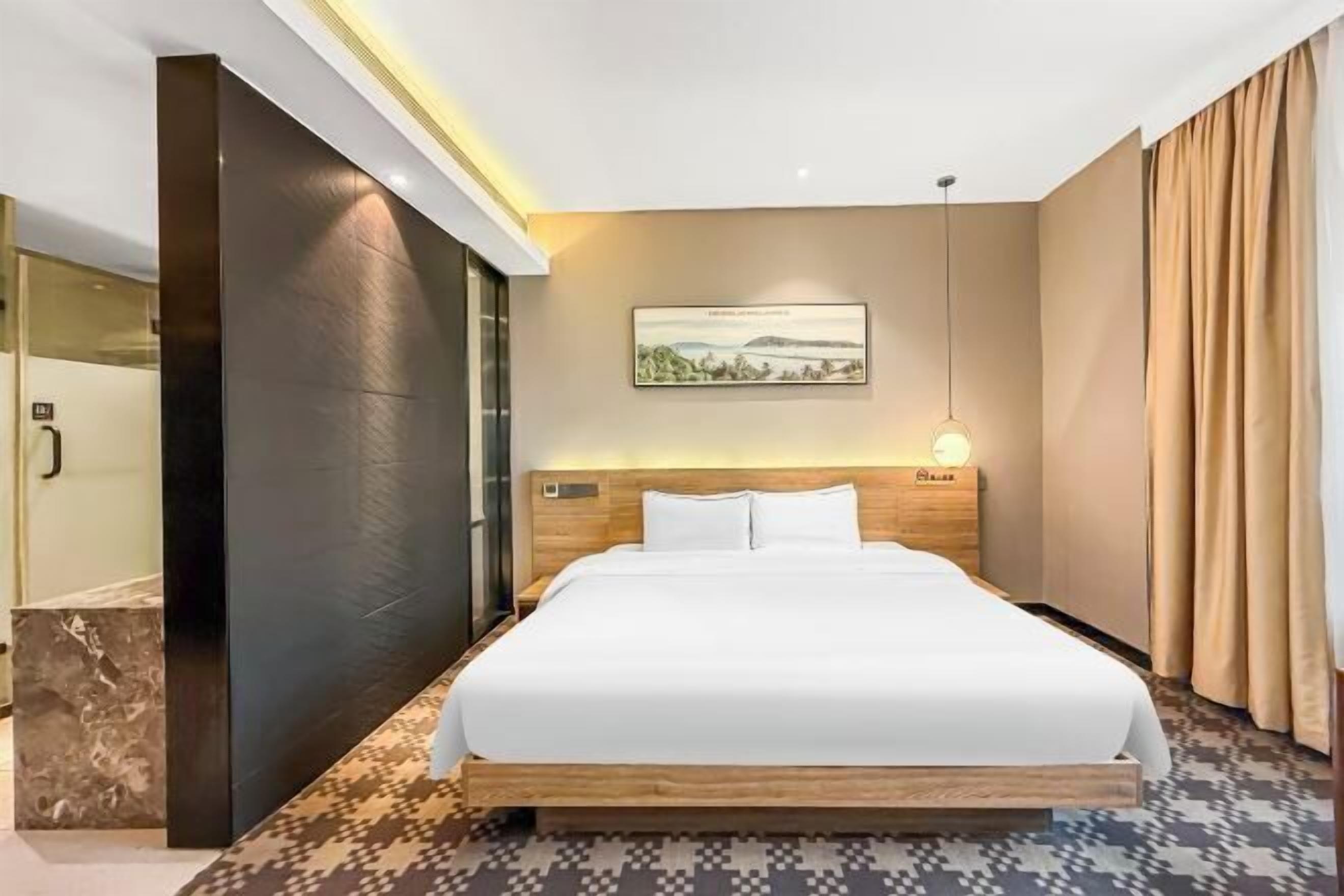 Una habitación de hotel con una cama, un cuadro en la pared, una mesita de noche y una ventana con cortinas.