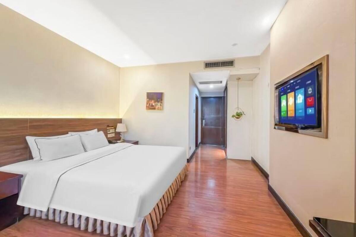 A hotel room with a bed, a TV mounted on the wall, and a hallway leading to a staircase.