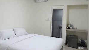 Un dormitorio con cama, aire acondicionado, una puerta, un mueble pequeño y un par de zapatos.