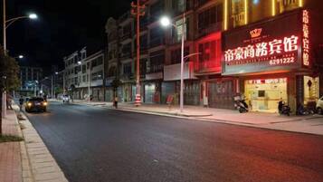 Vista da rua à noite com vitrines iluminadas, incluindo um hotel com uma placa chamativa.