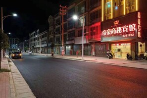 Vista d'un carrer de nit amb botigues il·luminades, incloent-hi un hotel amb un cartell ben visible.