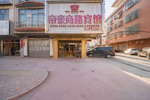 Entrada de un hotel con un letrero, una tienda cerrada y coches aparcados.