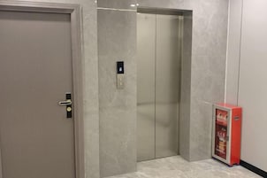 Un ascensor con pantalla digital, una puerta con manija y un cartel publicitario rojo.