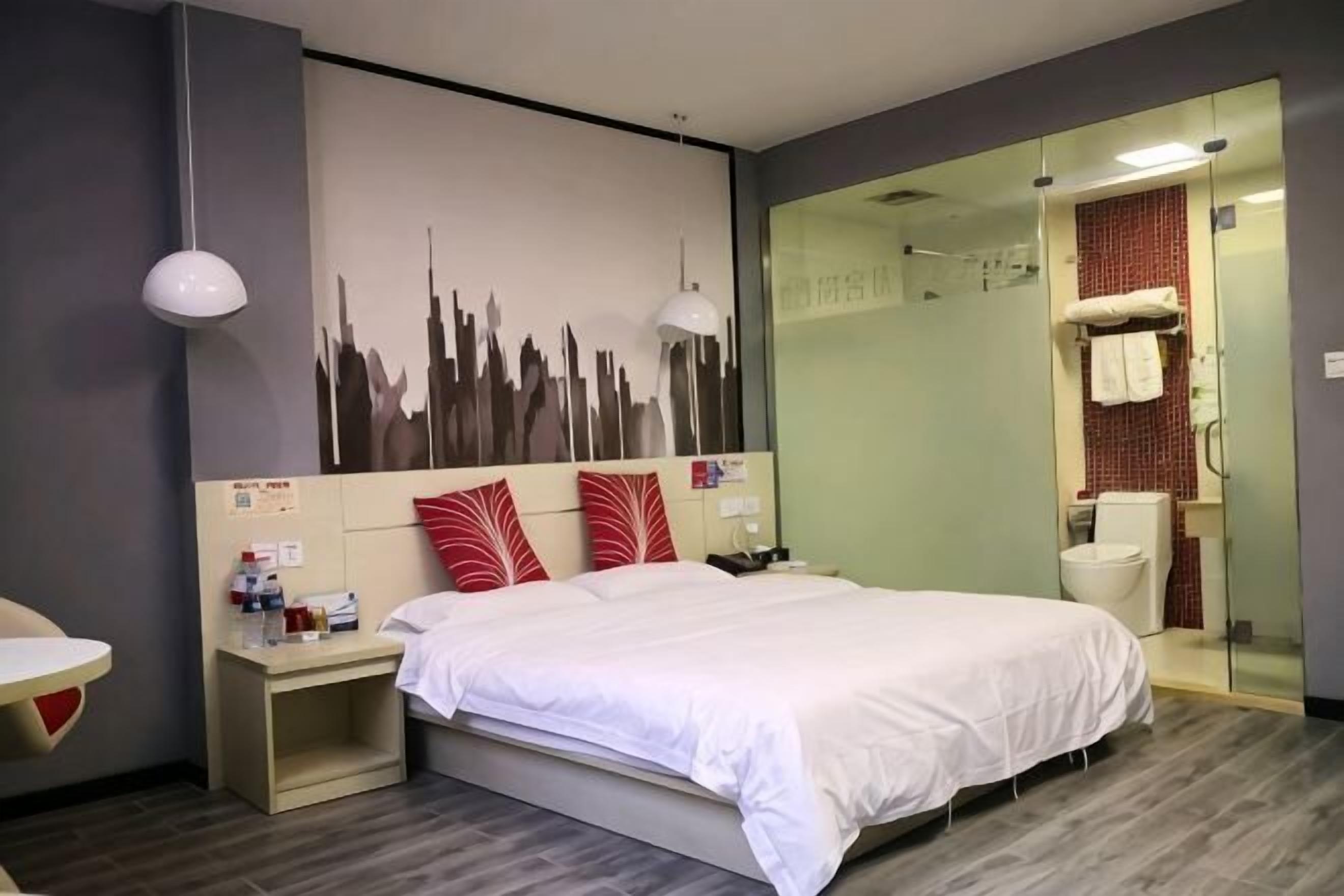 Una habitación de hotel moderna con cama, mesitas de noche, un mural con vista a la ciudad, cabina de ducha de vidrio y un inodoro.
