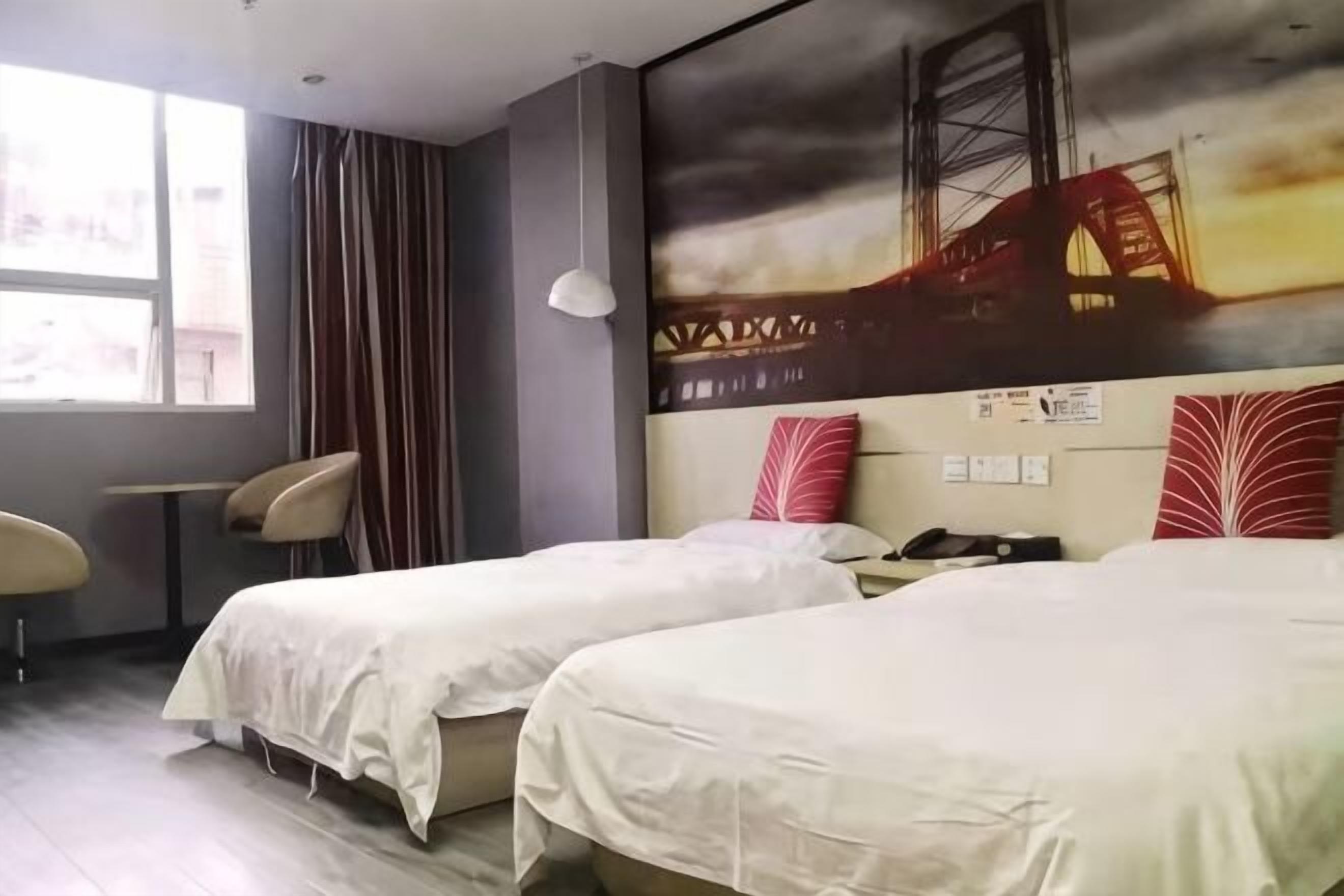 Una habitación de hotel con dos camas, un escritorio, una silla y un ventanal grande.