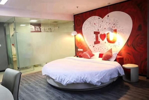 A modern bedroom with a circular bed, a glass partition wall, and a heart-shaped wall decoration.