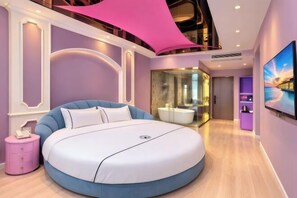 Un dormitorio moderno con una cama redonda, una pared de acento rosa y un amplio ventanal.