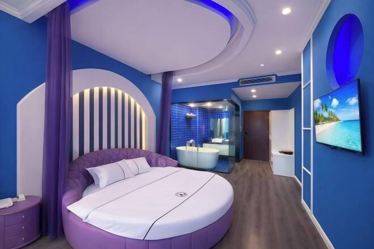 A modern bedroom with a circular bed, a bathroom with a bathtub, and a TV on the wall.