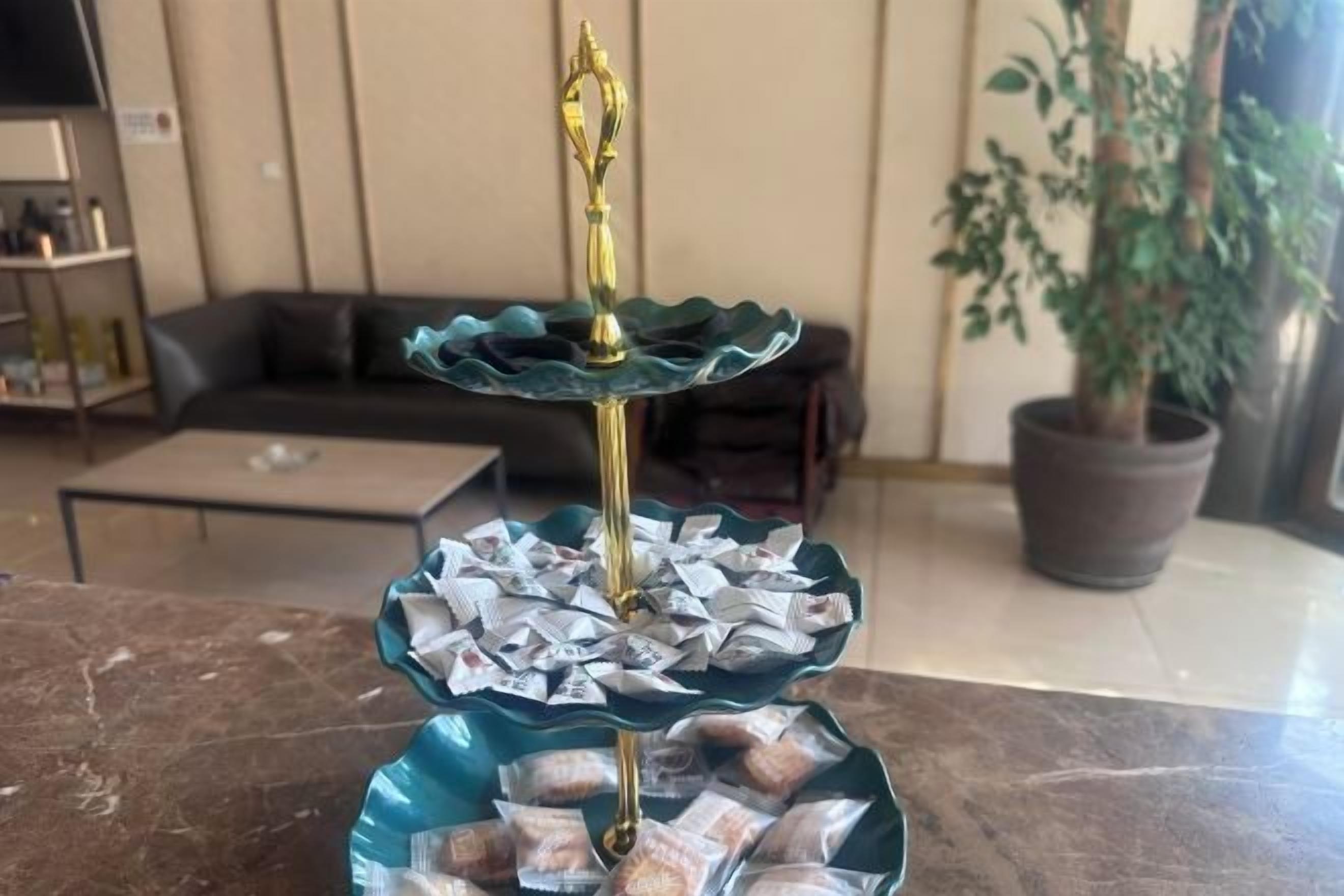 A dining table with a decorative centerpiece featuring a tiered stand with a golden top and a blue base, surrounded by wrapped food items.