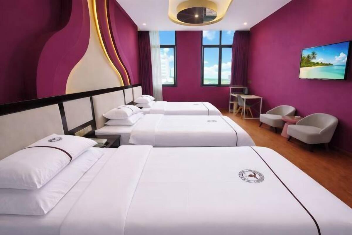 A hotel room with two beds, a desk, chairs, and a TV.