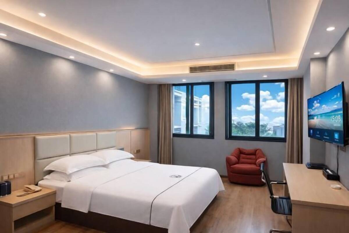 A hotel room with a bed, a desk, a chair, a TV, and large windows.