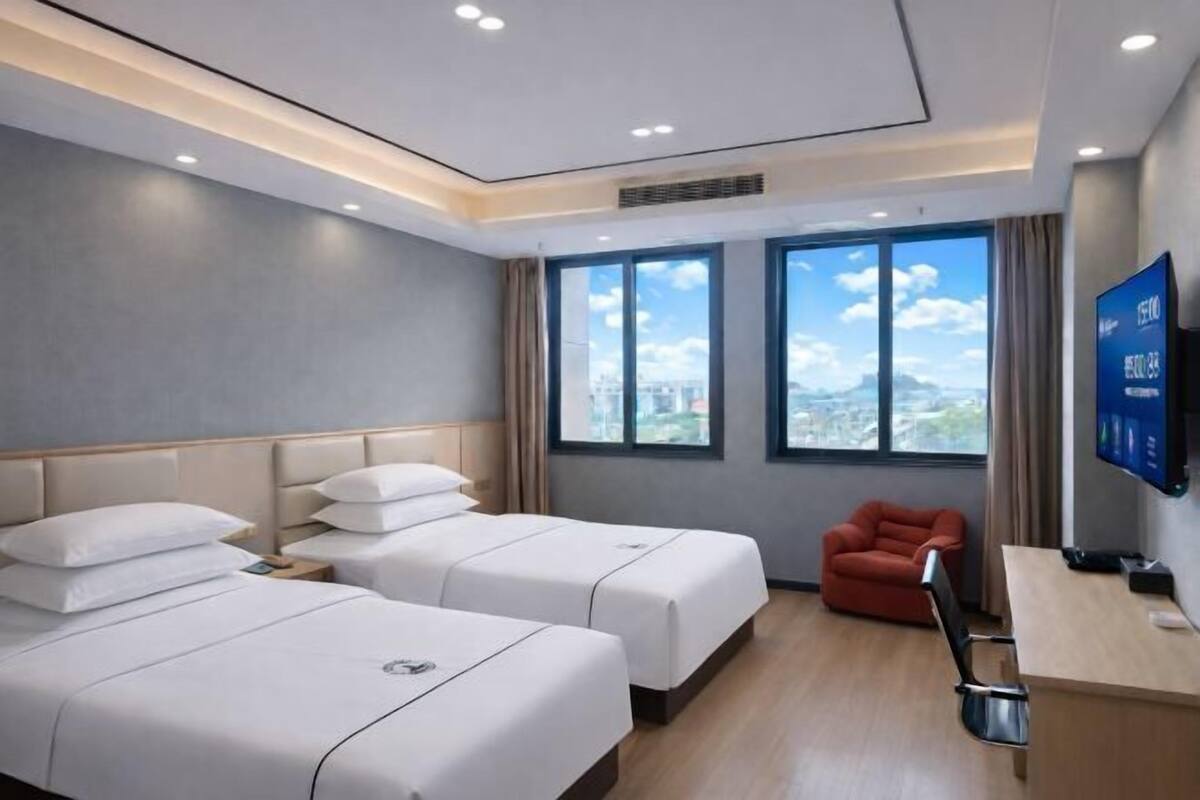 A hotel room with two beds, a TV, a desk, and a view of the city.