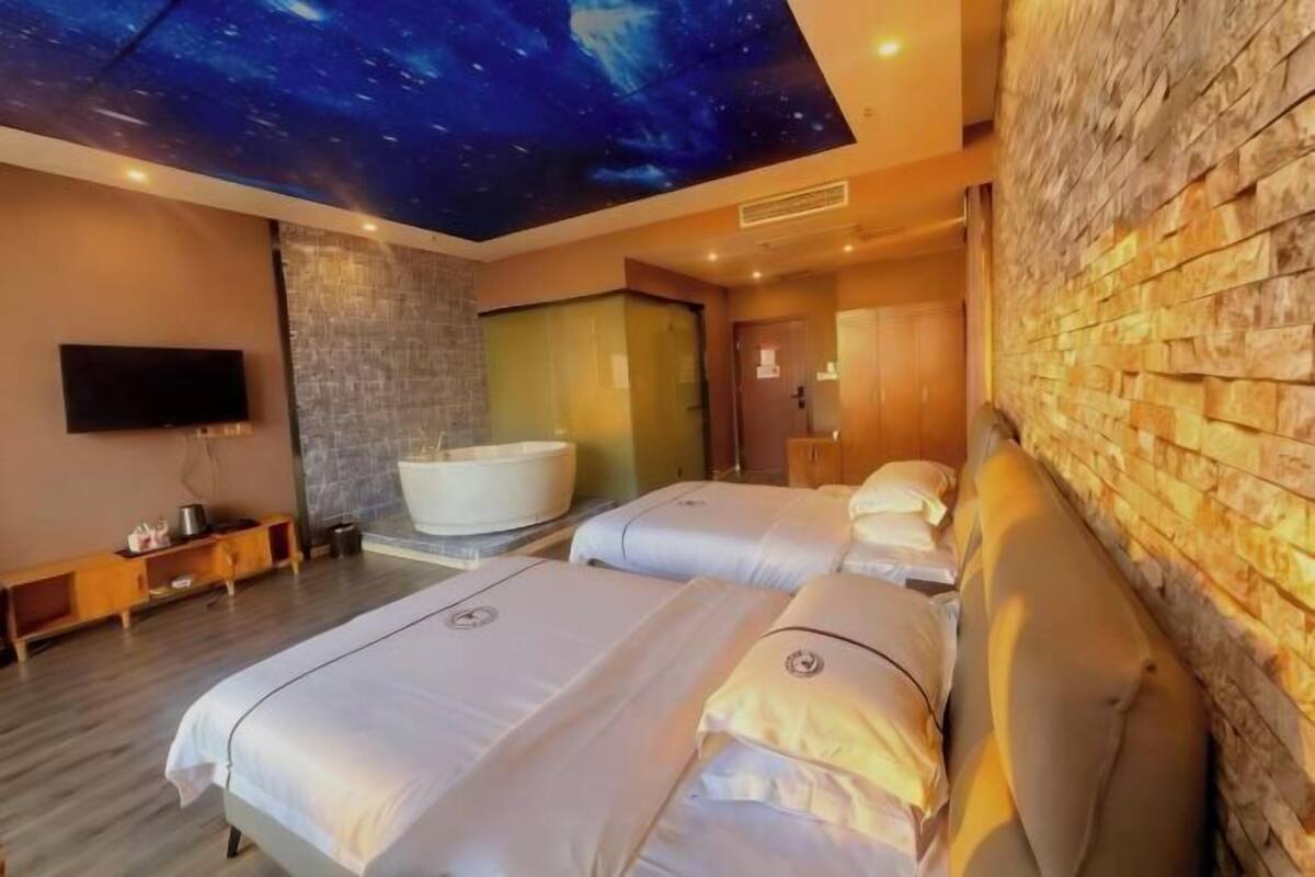 A hotel room with two beds, a large bathtub, a flat-screen TV, and a starry ceiling design.
