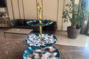 A three-tiered decorative stand with a golden top, filled with wrapped items, placed on a marble surface in a room with a sofa and potted plants.
