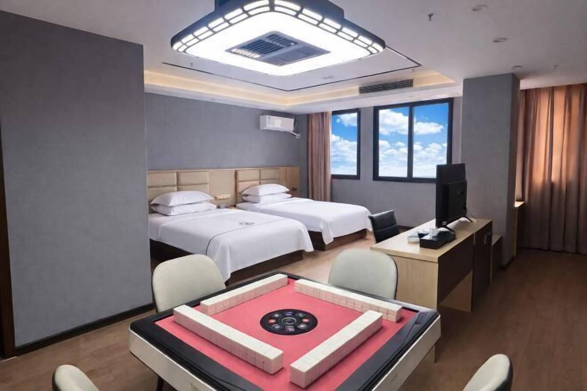 A hotel room with two beds, a desk with a computer, a television, and a large window with a view of the sky.