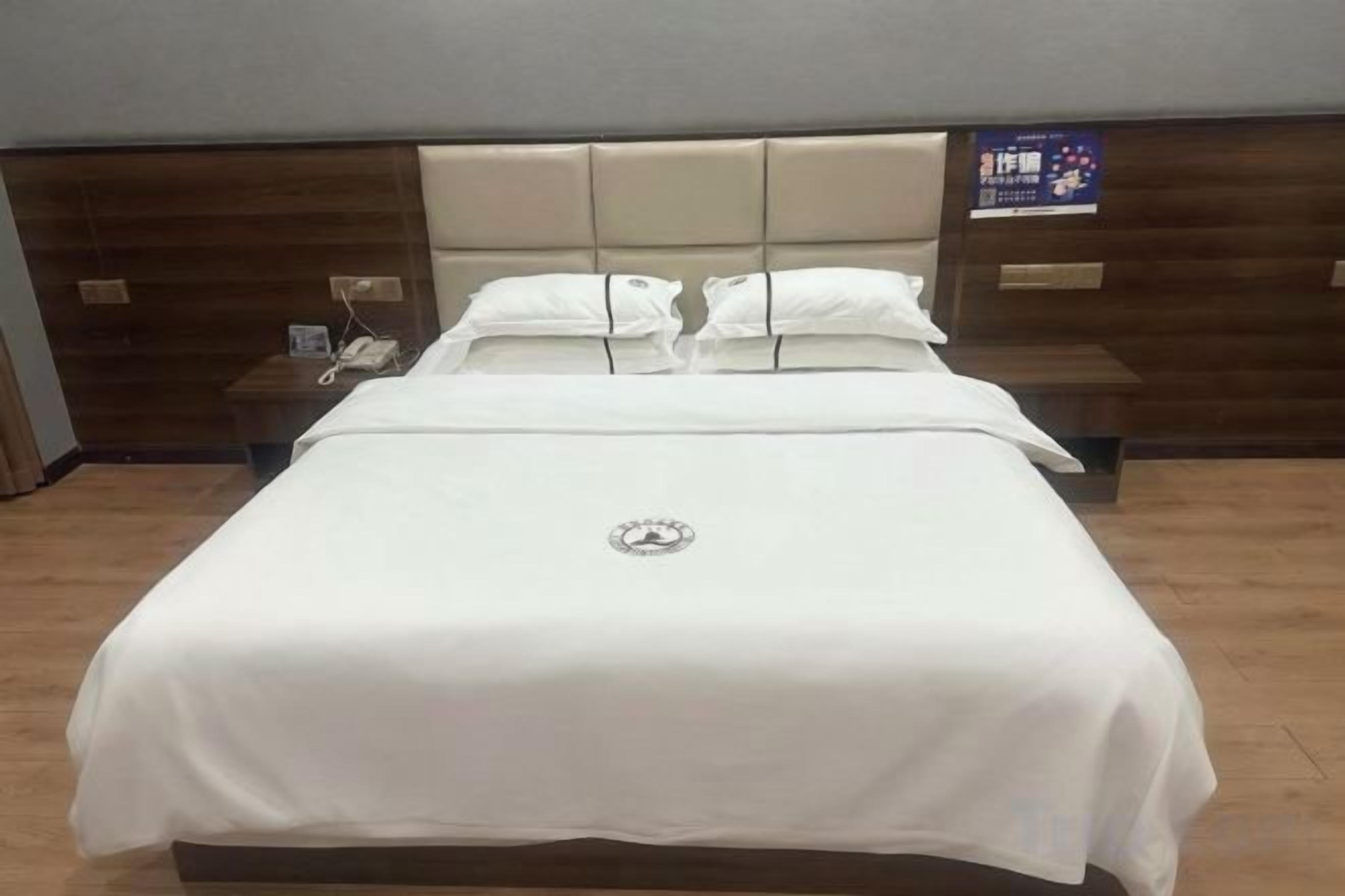 A hotel room with a large bed, a headboard, a bedside table, and a wall-mounted phone.