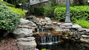 A stone waterfall in a landscaped garden with dense foliage and a stone wall.