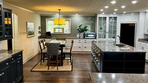 A modern kitchen with a dining area, featuring a central island, dark cabinetry, and a large window with a view.