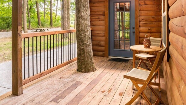 A wooden cabin with a porch, a door, and a small table with chairs.