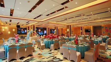 Un salón de banquetes con mesas redondas, sillas y un escenario.