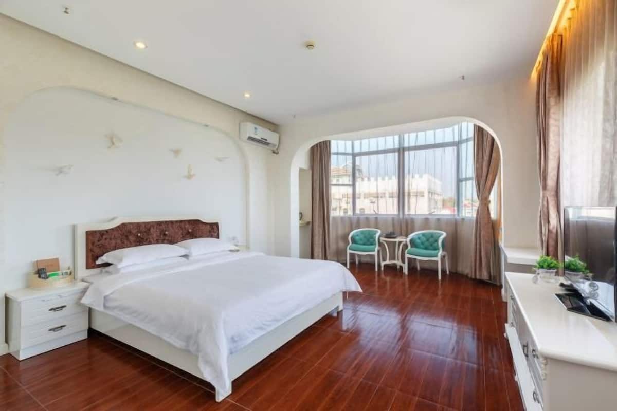 A hotel room with a bed, bedside table, two chairs, a desk, and a large window.