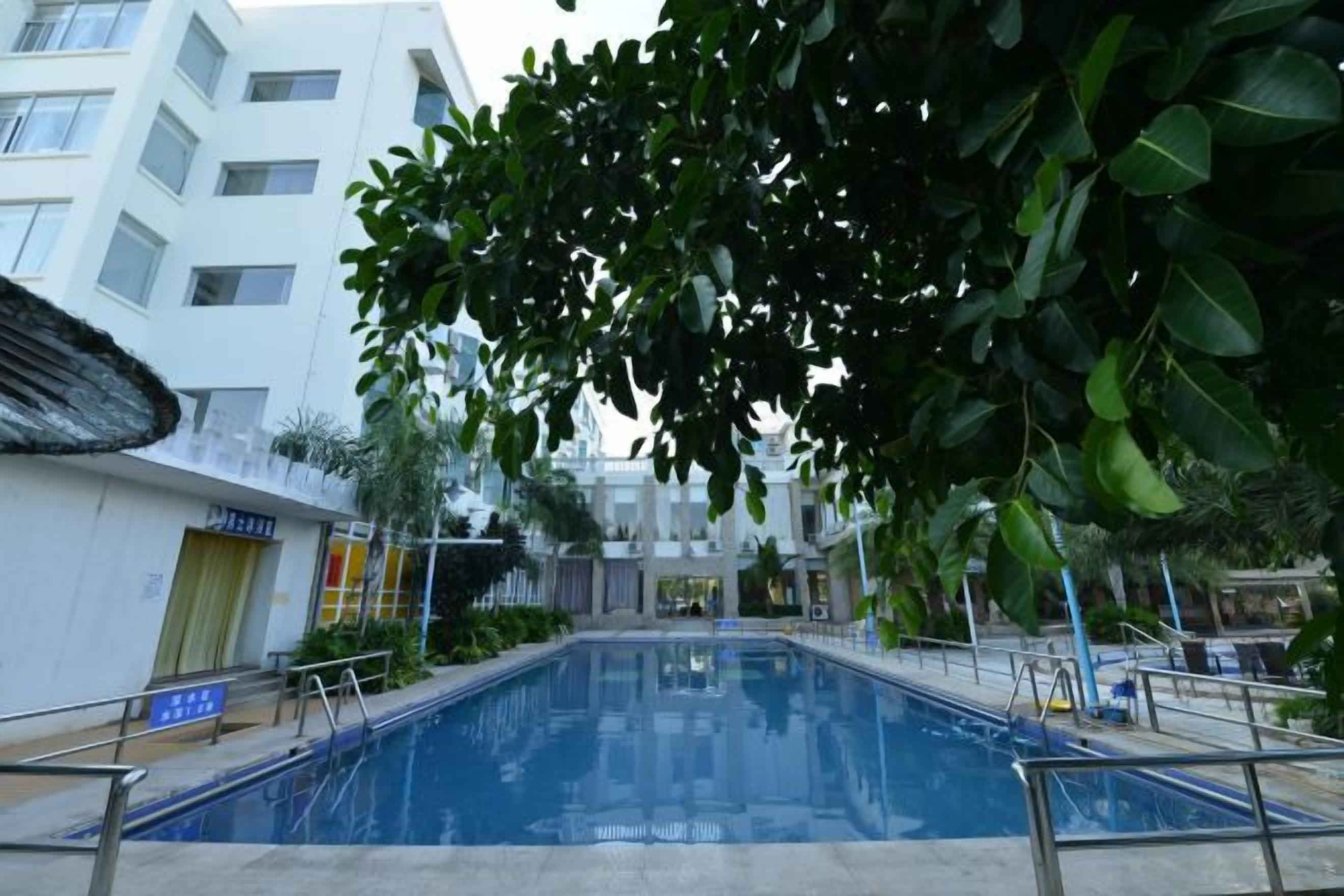 A swimming pool with a metal railing, surrounded by greenery and a building with multiple floors.