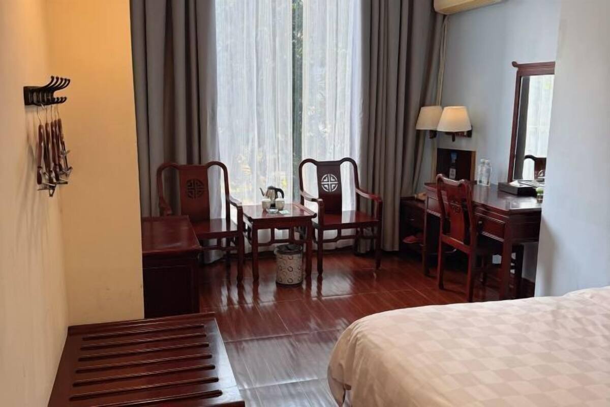 A hotel room with a bed, a desk with a chair, a small table, and a mirror.