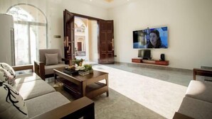 Un ampio soggiorno con una grande TV a schermo piatto montata a parete, un comodo divano, un tavolino da caffè e una porta in legno che dà su un'altra stanza.