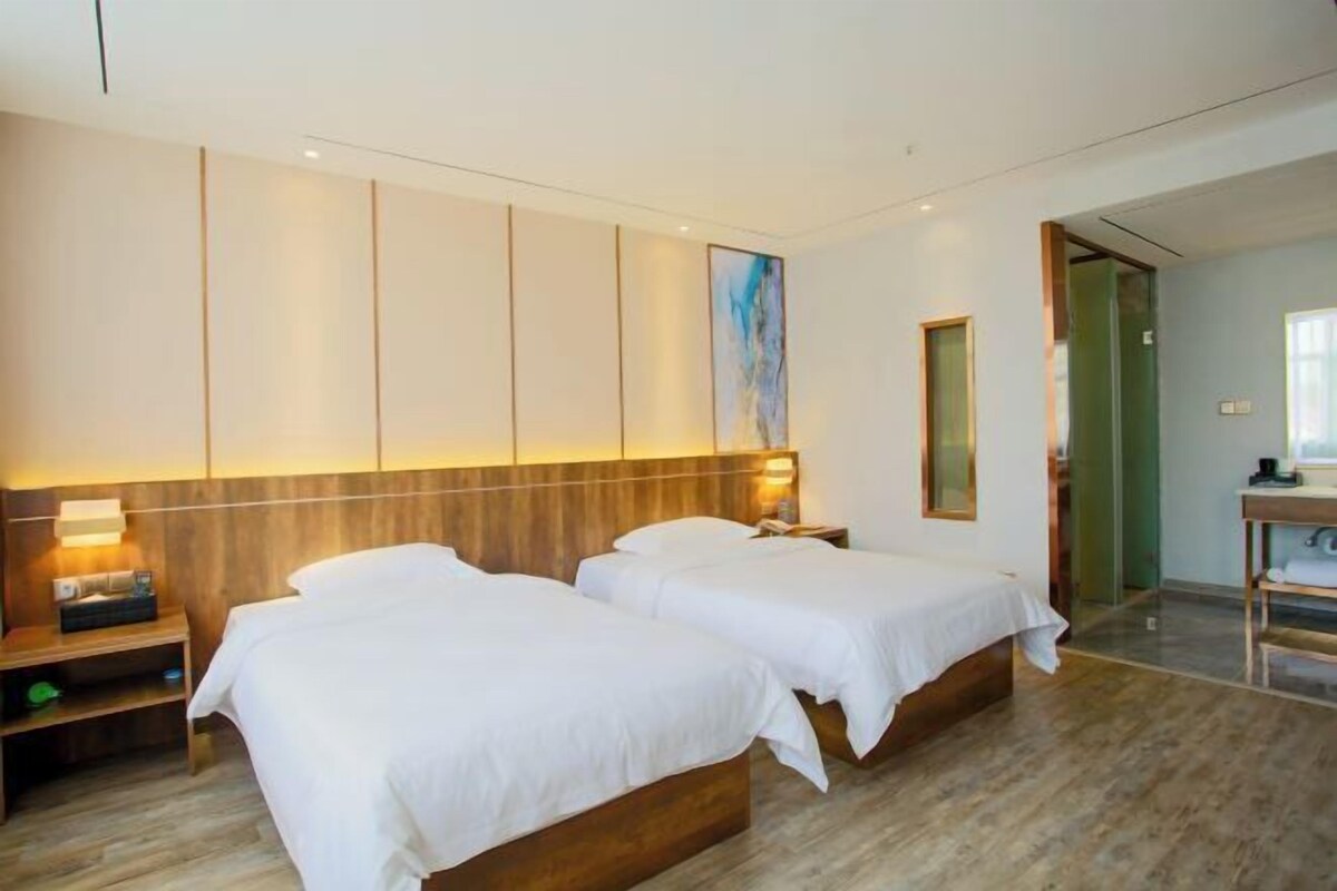 Une chambre d’hôtel avec deux lits, une tête de lit en bois, une table de chevet avec une lampe et un tableau au mur.