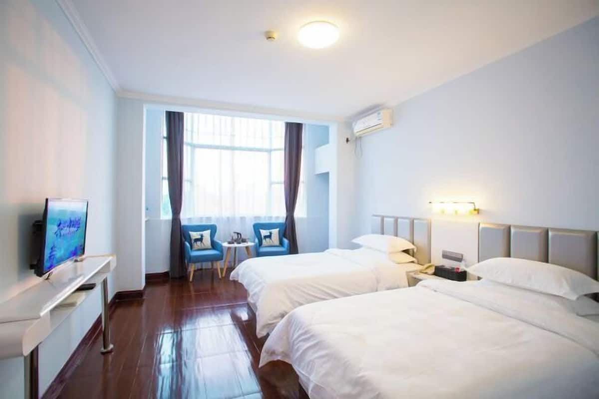 A hotel room with two beds, a TV, a desk, a chair, and a window with curtains.