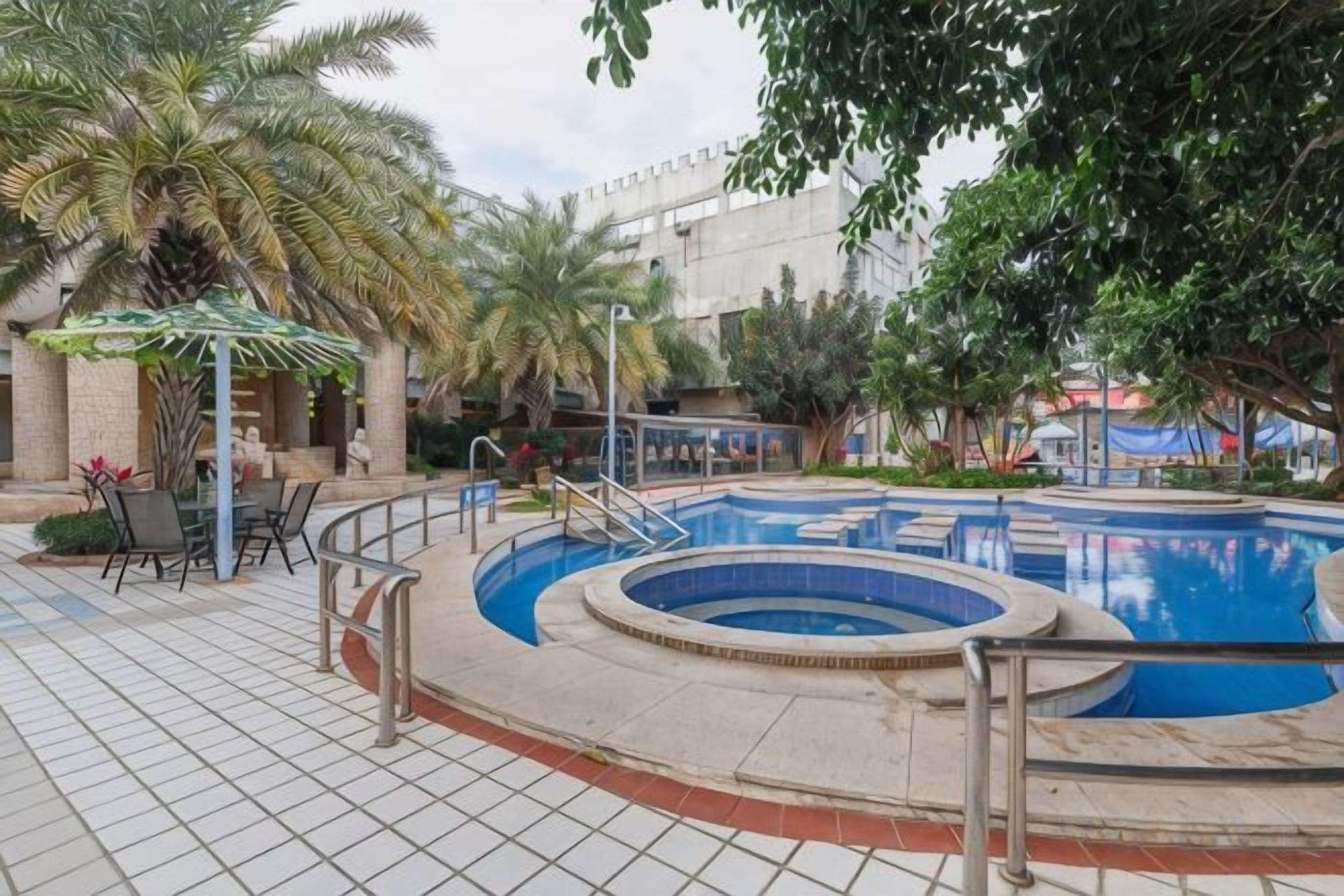 An outdoor swimming pool with a circular design, surrounded by palm trees and a tiled walkway.