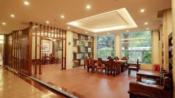 A spacious indoor area with a long corridor, a dining area with wooden furniture, and a large window providing a view of greenery.