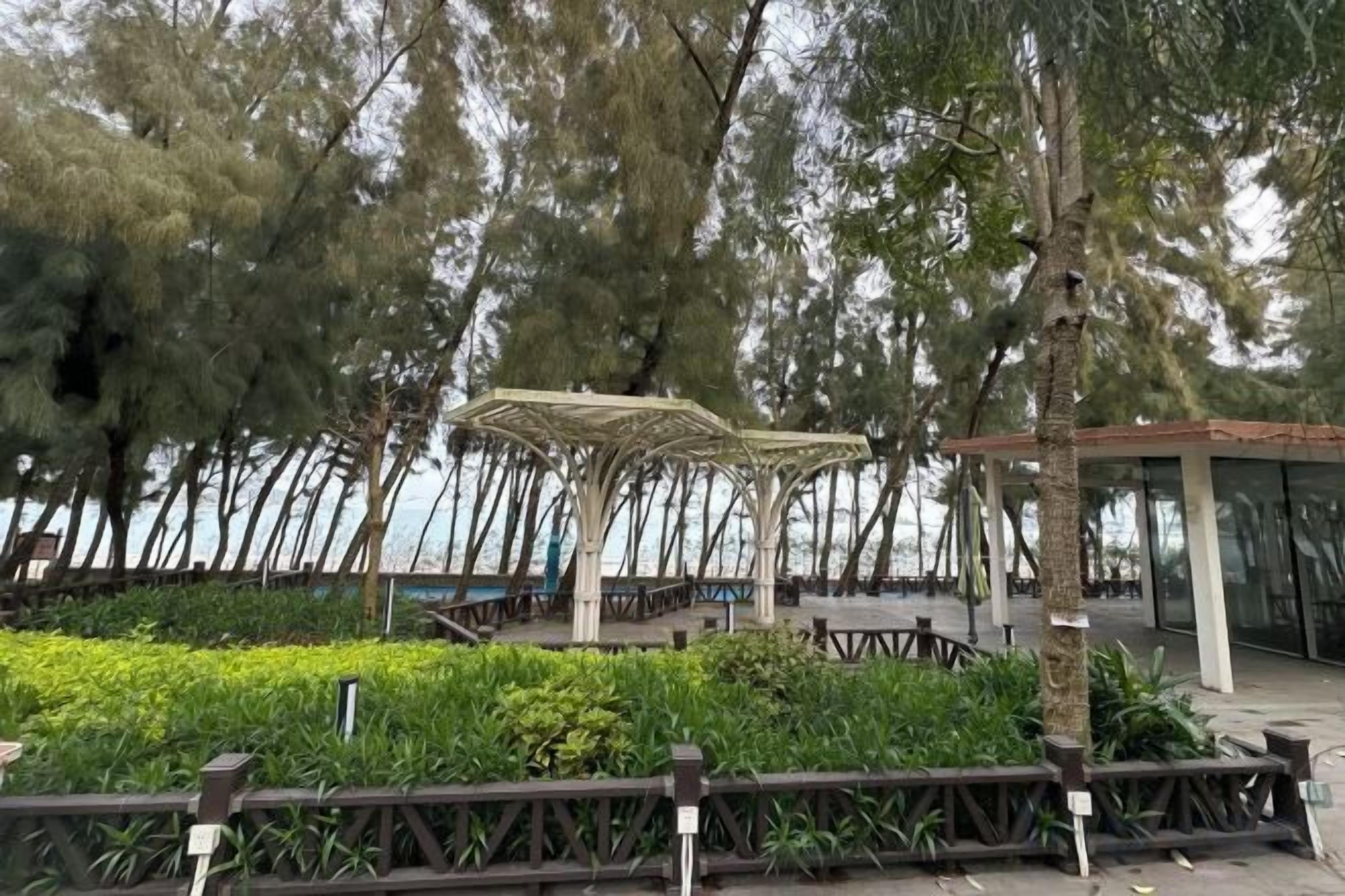 A gazebo with a roof structure, surrounded by greenery and trees.
