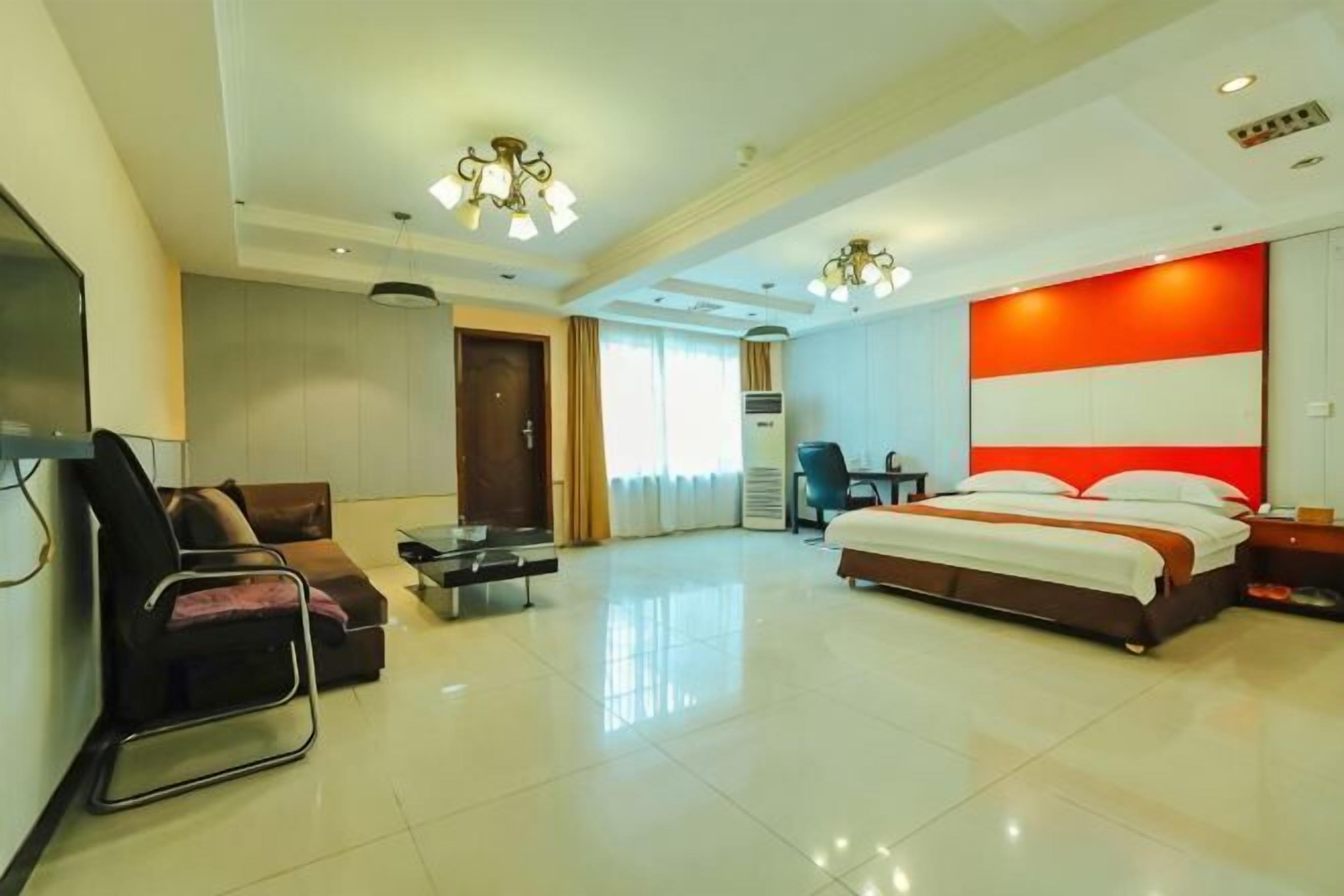 A hotel room with a bed, a desk, a chair, a TV, and a sofa.