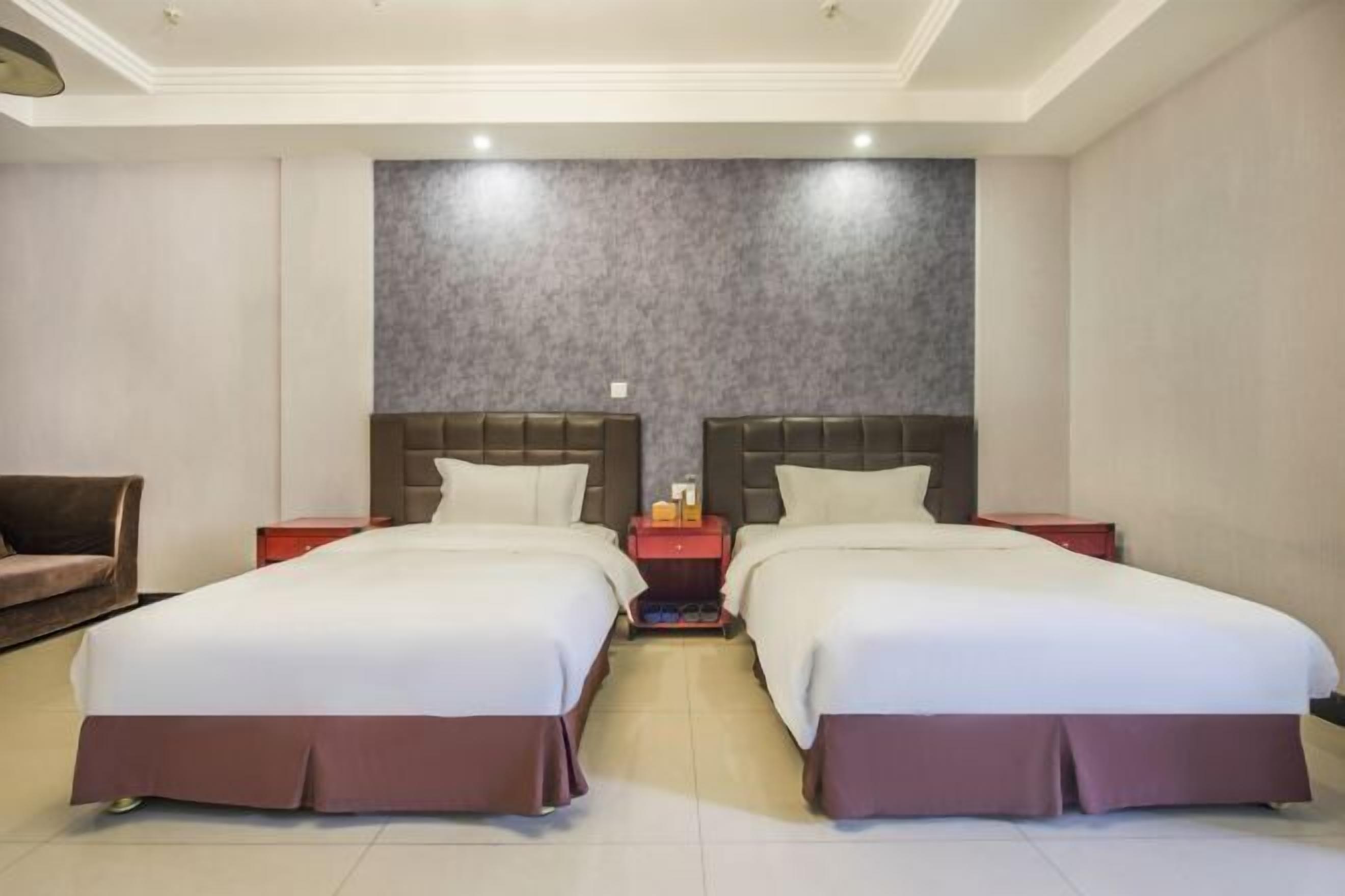 A hotel room with two beds, a sofa, and a nightstand with a lamp.