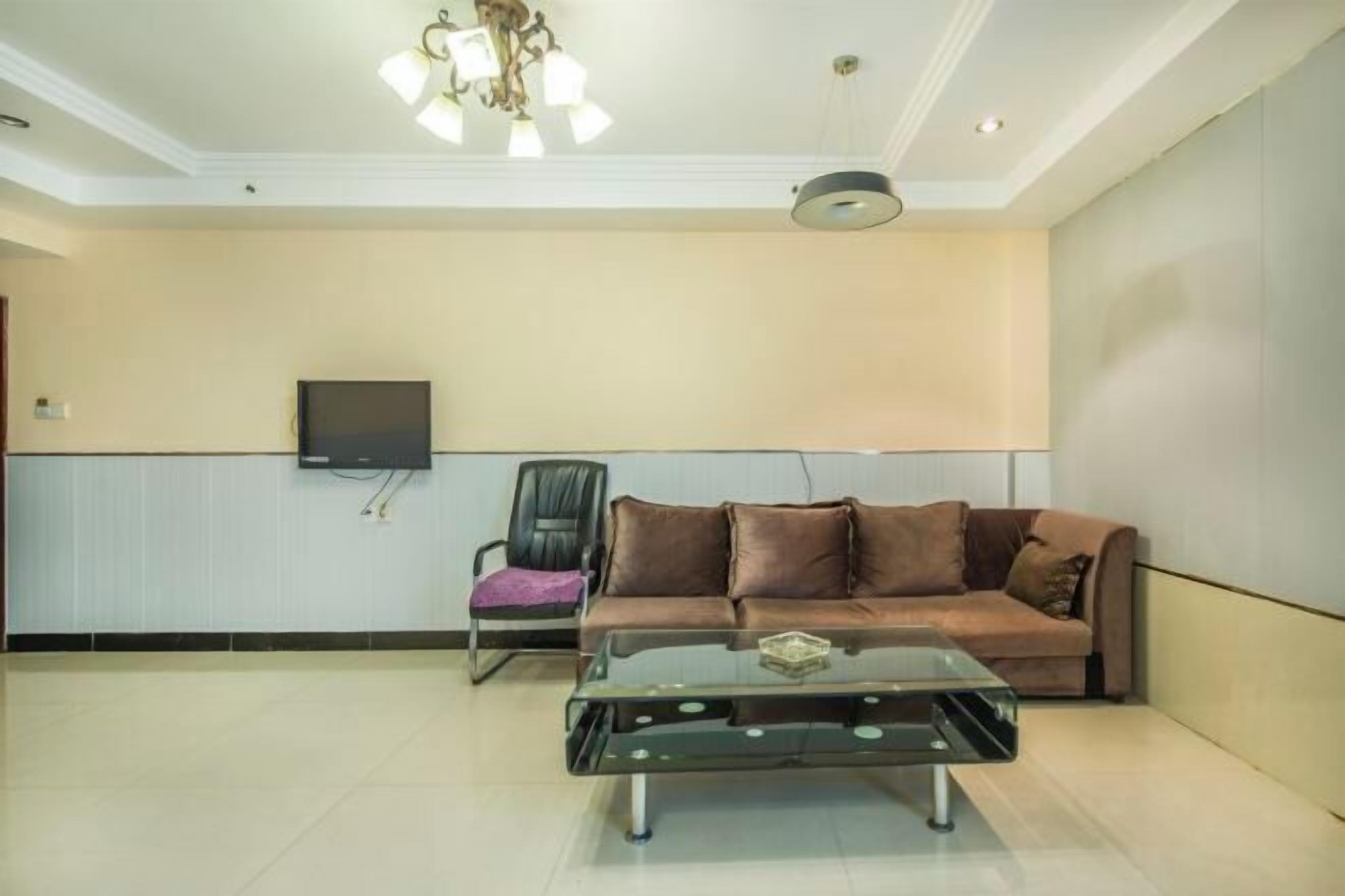 A living room with a sofa, a glass coffee table, a TV mounted on the wall, and a ceiling light fixture.