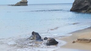 Une plage avec un ciel dégagé, une eau calme et des formations rocheuses.