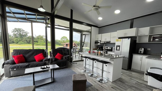 A modern kitchen with a central island, bar stools, and a dining area with a sofa and coffee table.