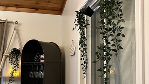 Ein Zimmer mit Holzboden, einem Fenster mit der Aufschrift 'CHARDONNAY', einer schwarzen, gewölbten Vitrine und einer hängenden Pflanze.