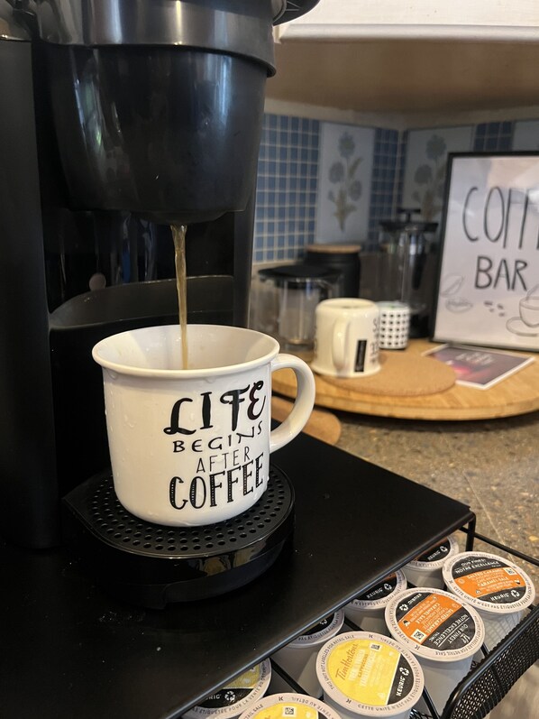 Una cafetera sirviendo café en una taza, con el texto “LITE BEGINS AFTER COFFEE” en una estación de café negra con varios pods de café.
