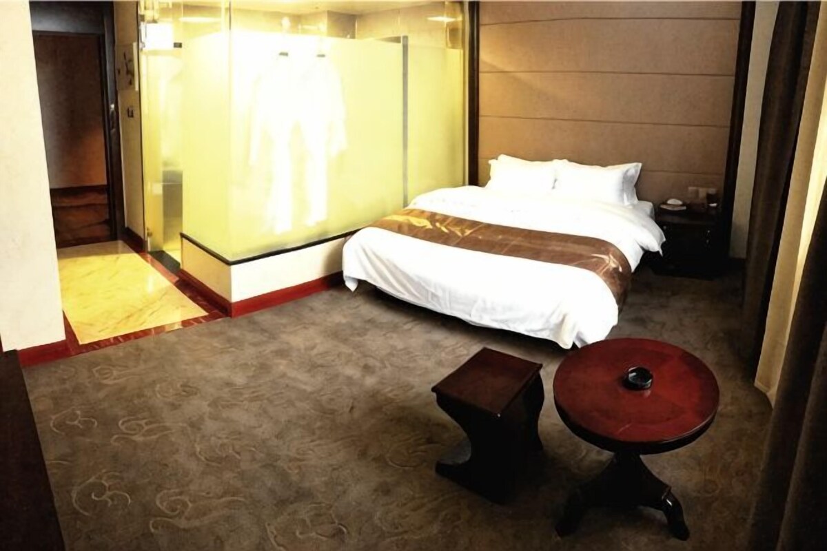 A hotel room with a bed, a small table, a mirror, and a wardrobe.