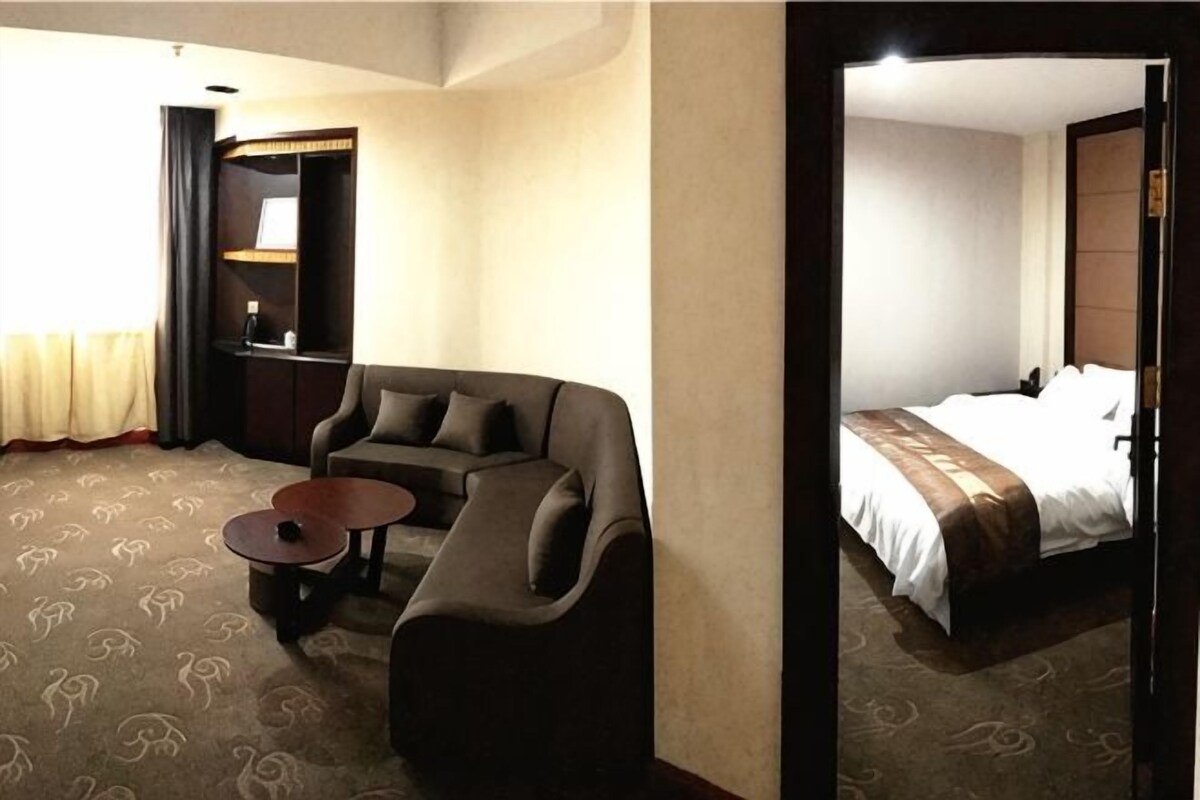 A hotel room with a bed, a sofa, a small table, and a mirror.