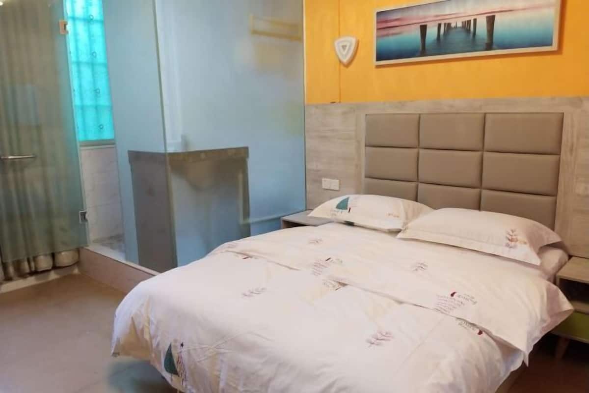 A hotel room with a bed, a headboard, a shower area, and a painting on the wall.