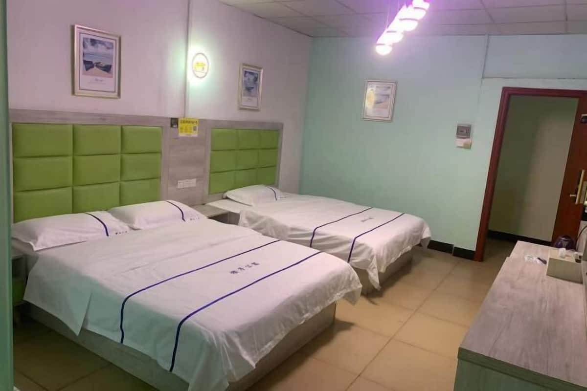 A hotel room with two beds, a wooden desk, and a door.