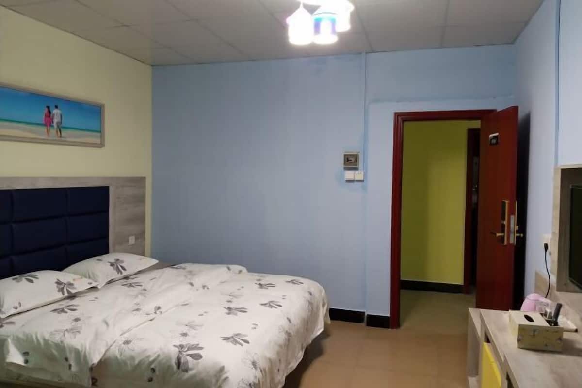 A bedroom with a bed, a nightstand, a painting on the wall, and a door leading to another room.