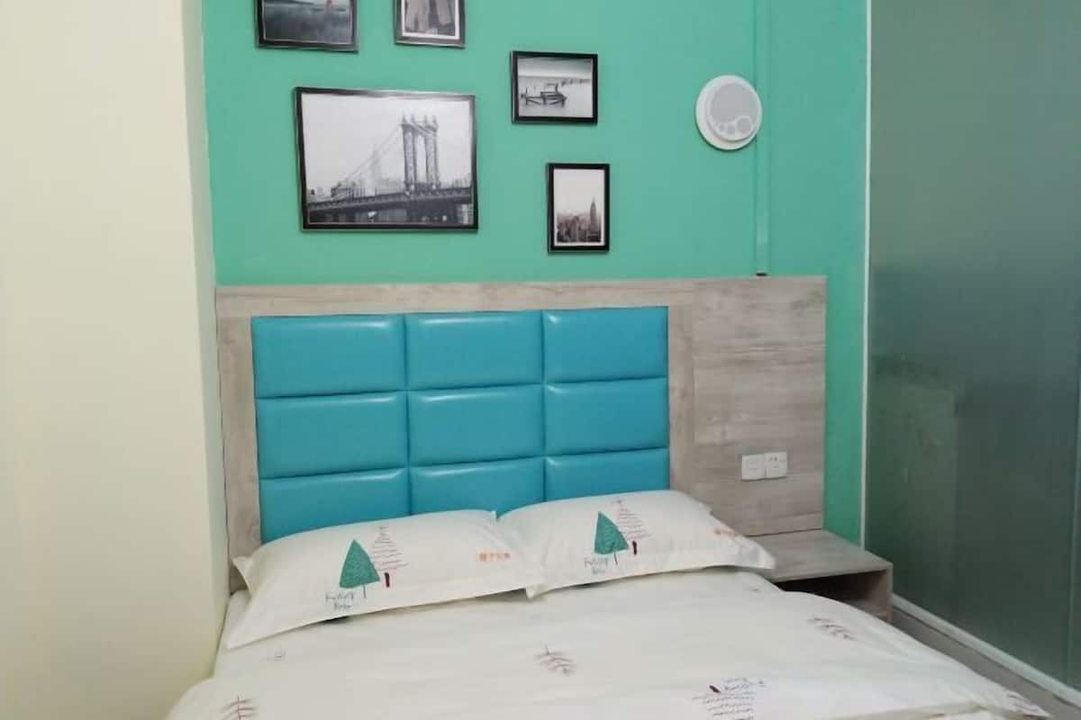 A room with teal walls, a bed with white bedding and teal pillows, and a headboard with a light wood finish.