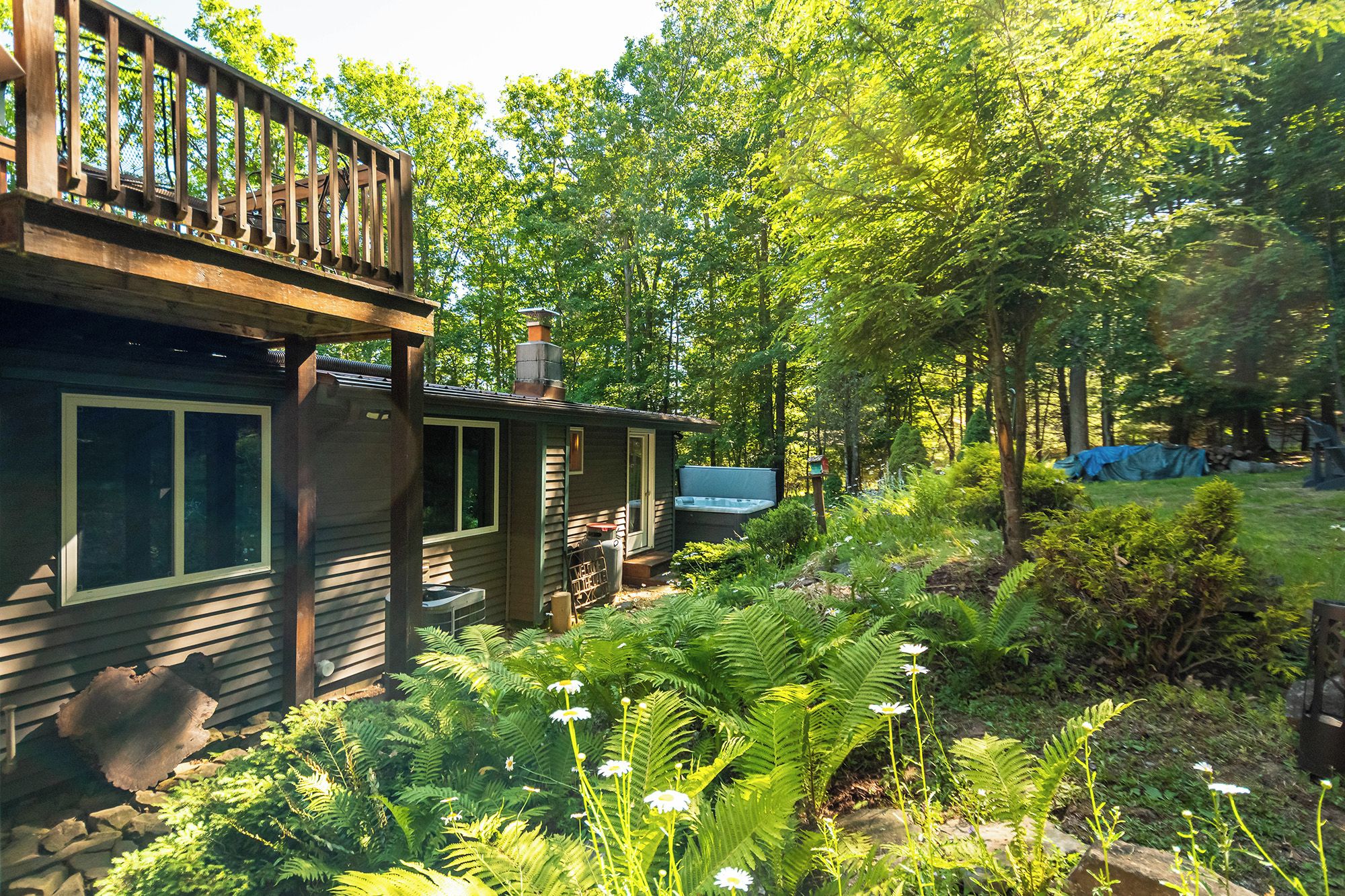 A cabin with a deck, surrounded by dense greenery and a hot tub.