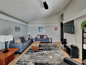 Ett modernt vardagsrum med en soffgrupp, ett soffbord, en tv och en bokhylla.