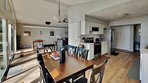 Una cocina moderna con armarios blancos, microondas y refrigerador. Hay un comedor con mesa y sillas de madera.